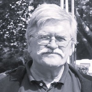 Ein schwarz-weiß Bild. Ein älterer Mann mit Brille schaut in die Kamera.